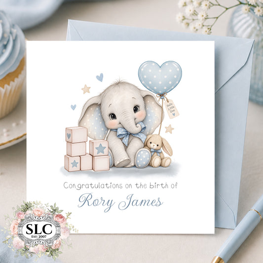 A personalized baby birth announcement card featuring a cute cartoon elephant and bunny with a blue polka-dot balloon, shown with a light blue envelope on a styled tabletop. The card reads 'Congratulations on the birth of Rory James' and includes an 'SLC Est.