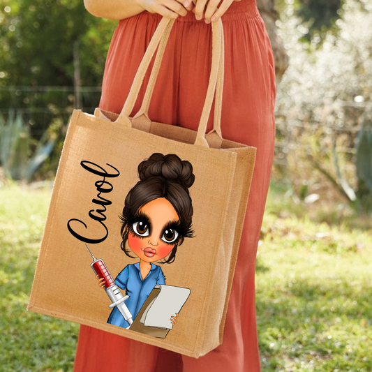 A person in a rust-colored dress holds a natural jute tote bag outdoors. The bag features a cartoon illustration of a woman with dark hair in a bun, wearing a blue scrub top, holding a syringe, and next to the name 'Carol' in black script.
