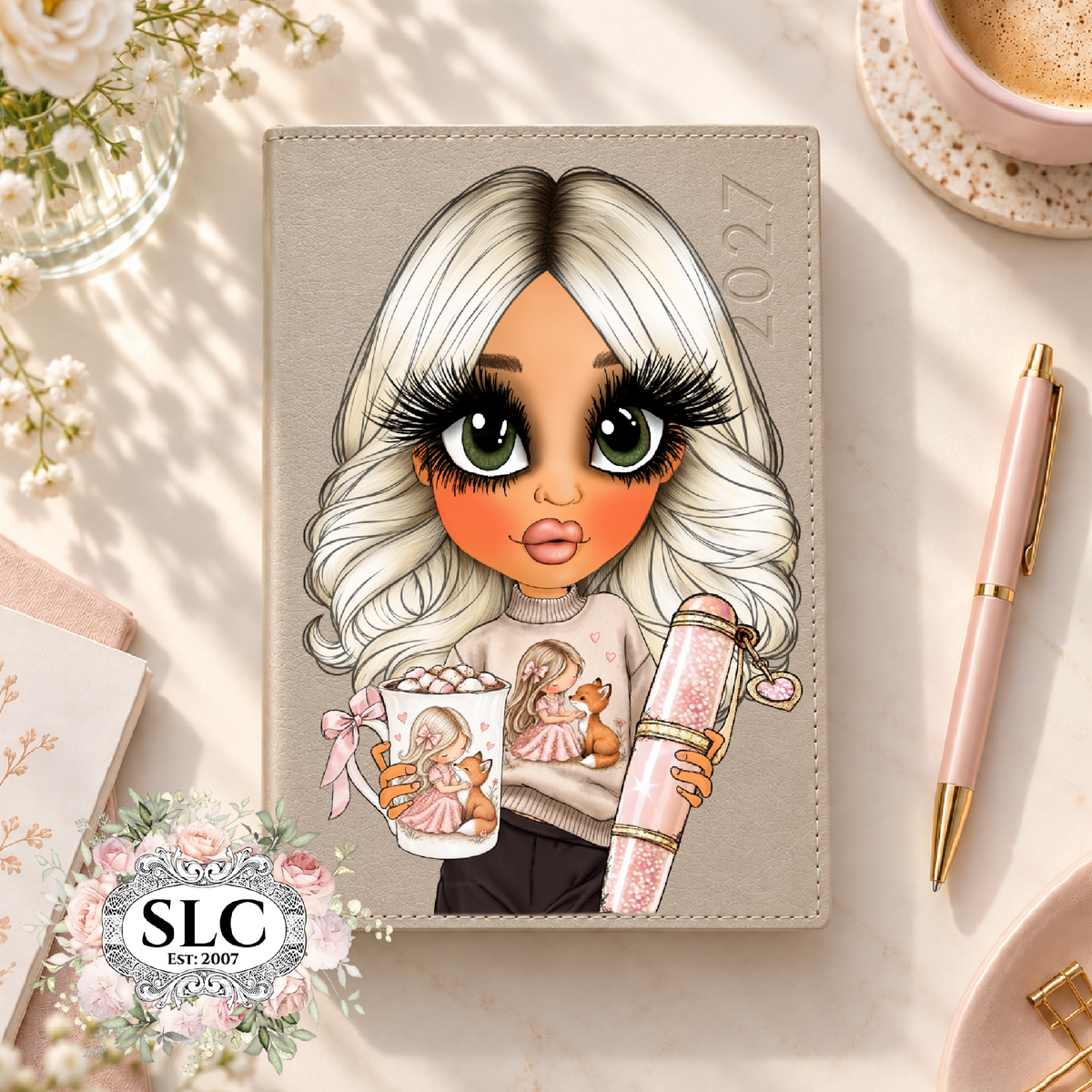 A personalized 2027 journal cover featuring a cartoon illustration of a girl with long white hair, large green eyes, and a pink dress, holding a cup and a glittery pink bottle. The cover is beige and shown in a styled flat-lay setting with a pink pen, a coffee cup, and flowers.