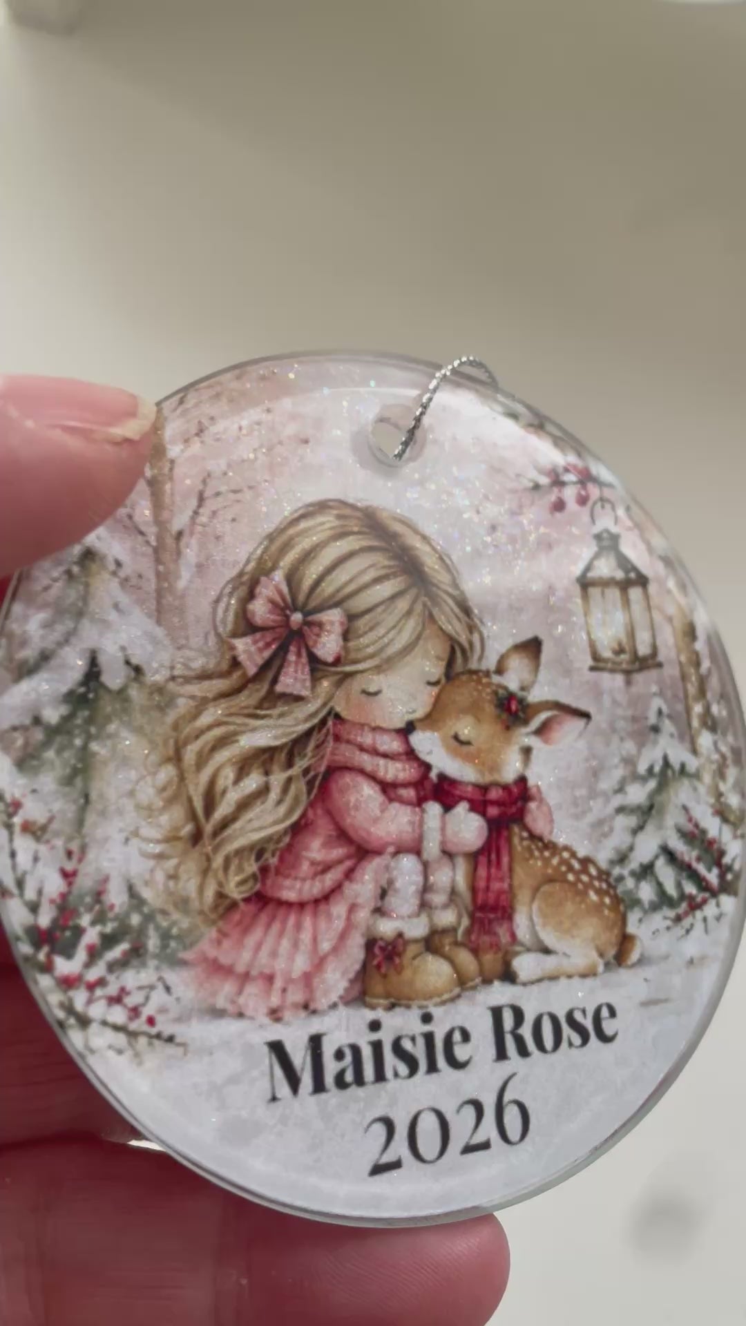 vieo showing a personalised glass tree decoraton with al illustrated pic of a little girl hugging a deer in snow scene